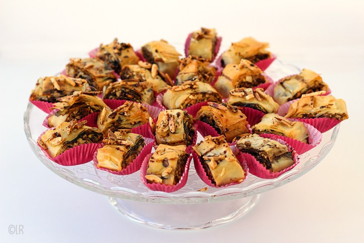 Oriëntal delight deze heerlijke baklava hapjes! Schaal met rolletjes baklava in rode papieren cakevormpjes.