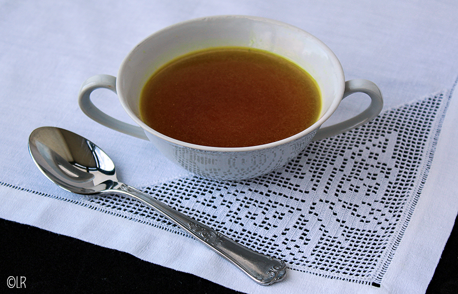 Bouillon - heerlijk, maar wat is nu waar en wat is fantasie.... Kopje geurige eigengemaakte bouillon op een kanten kleedje met een lepel ernaast.