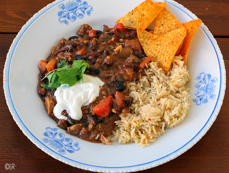 Mooi wit met blauw bord met Chili con carne geserveerd met een toefje zure room, wat koriander, rijst een paar taco's