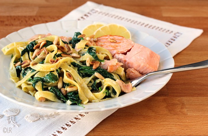 Het meest populaire stukje vis hier gepresenteerd met romige tagliatelle en spinazie. Bordje met een fraaie compositie van gebakken zalm met spinazie-tagliatelle en pijnboompitjes.