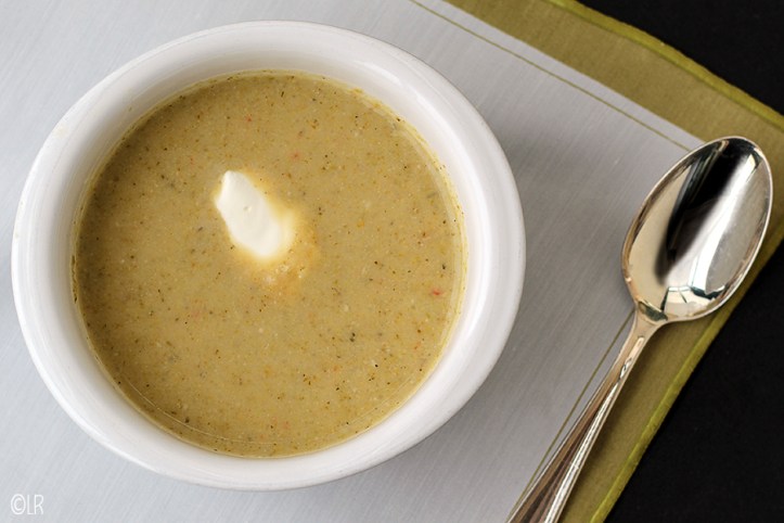 Heerlijk voedzaam soepje dat in een koolhydraatbeperkt dieet past. Kommetje romige broccolisoep met een klontje roomkaas en een zilveren soeplepel