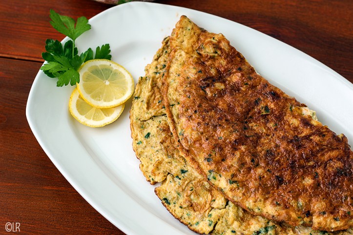 Schaal met een aan beide zijden bruin gebakken omelet met garnalen. Ernaast 2 schijfjes citroen en wat platte peterselie.