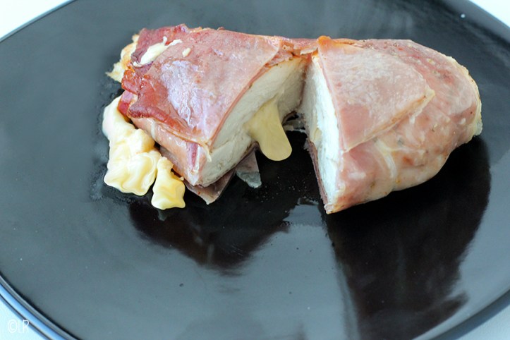 Opengesneden kipfilet omwikkeld met rauw ham. De gesmolten kaas uit het midden loopt eruit.
