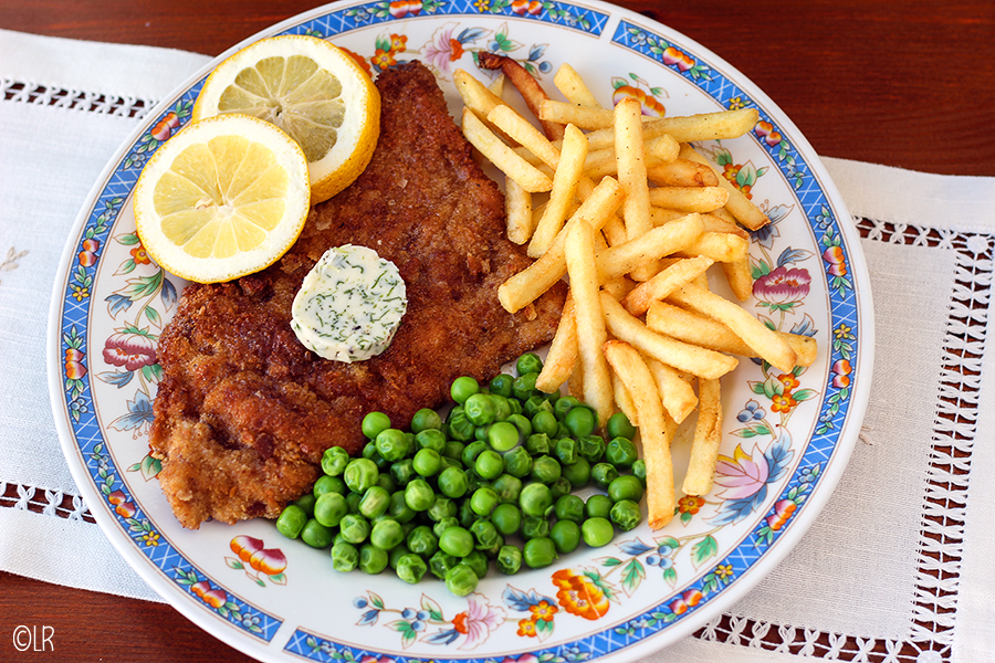 Bord met Wiener Schnitzel, tuinkers-boter, citroen met friet en doperwtjes.