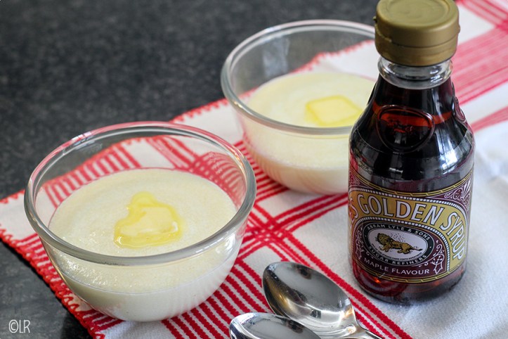 Twee schaaltjes griesmeelpap met een klontje goudgele roomboter en een flesje Golden Syrup ernaast.