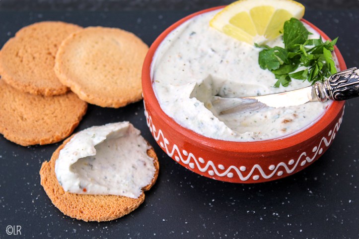 Schaaltje eigengemaakte kruidenkaas met erop een toefje peterselie en een schijfje citroen. Ernaast enkele toastjes.