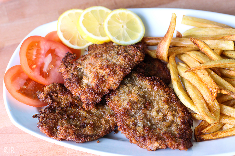 Gepaneerde gemarineerde varkenslapjes met tomaat, citroen en frietjes.
